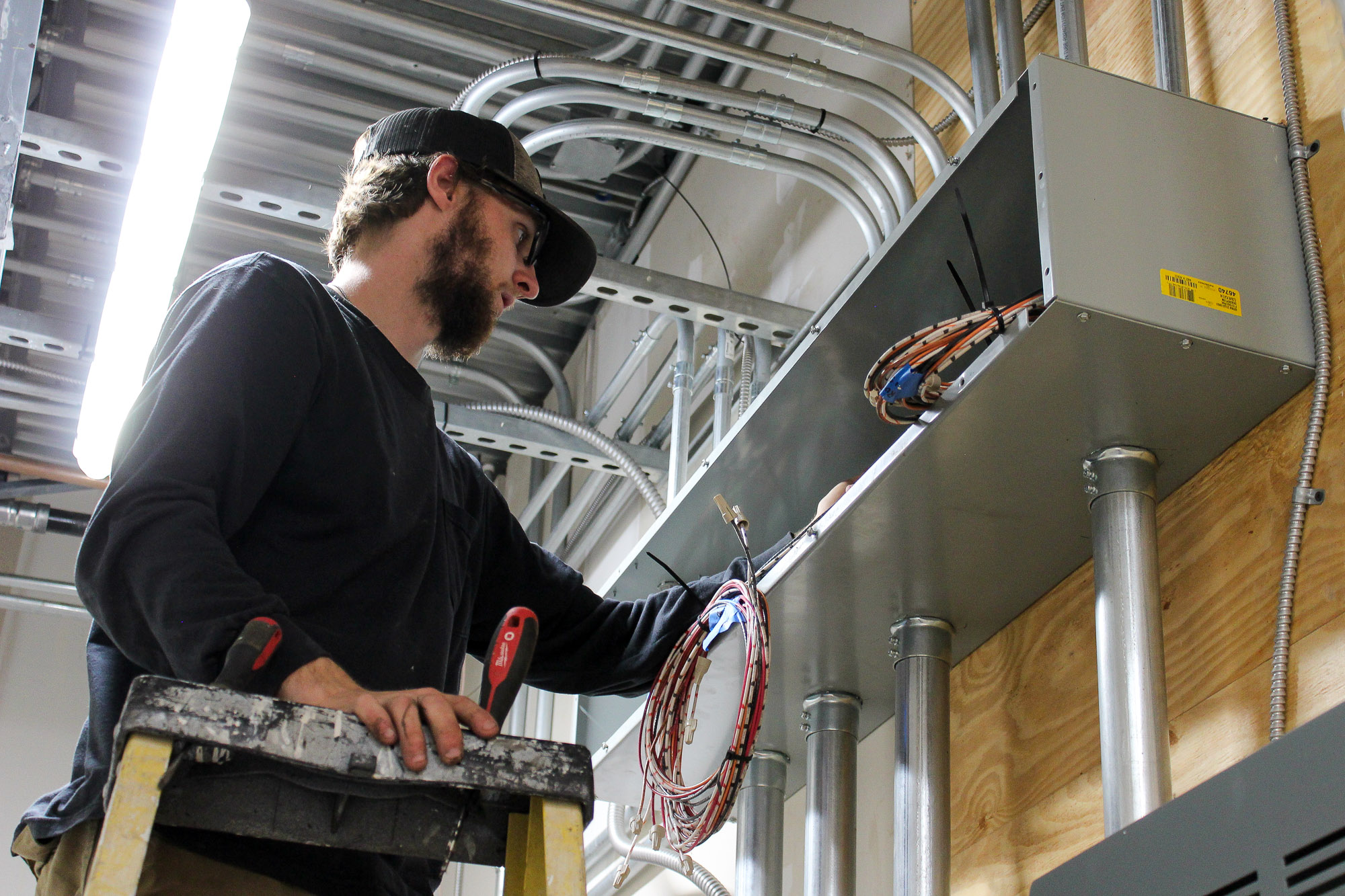 Electrician on a ladder running commercial wiring in a newly constructed commercial building, demonstrating professional electrical craftsmanship and safety compliance.